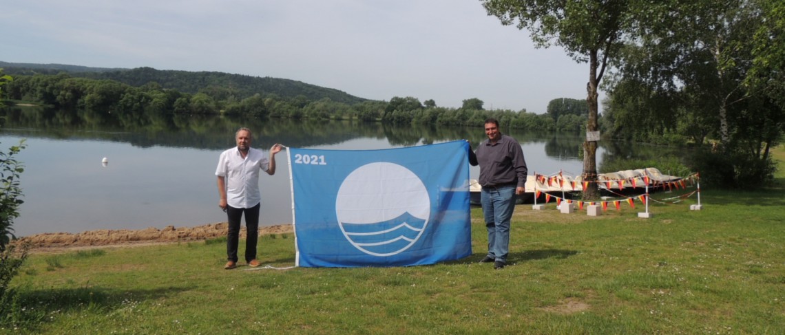 Personen halten eine Flagge hoch. Im Hintergrund See